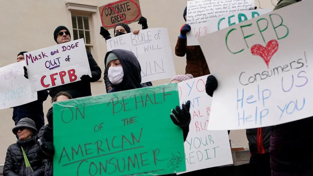 Demonstrators hold signs during a protest outside the Consumer Financial Protection Bureau on Saturday